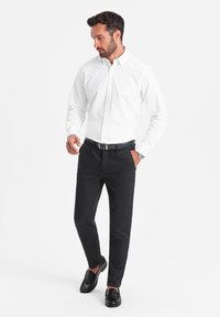 Chemise blanche à boutons, pantalon noir et mocassins noirs. La chemise est à manches longues et le pantalon a une coupe slim.