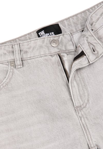 Jeans de mezclilla gris claro con cremallera parcialmente abierta, botón de metal, bolsillos cosidos y etiqueta de marca negra visible dentro de la cinturilla.