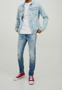 Ljusblå denimjacka över en vit t-shirt, ihop med slitna ljusblå jeans och röda sneakers. Funktioner inkluderar knäppta fickor och hål.