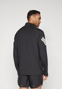 Sort atletisk langærmet bluse med høj krave, der har hvide tre-stribe detaljer på ærmerne og glat, letvægtsstof.