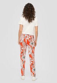 Pantalons à motifs rouges avec des motifs floraux blancs et bleus, associés à un haut crème à manches courtes. Présente des jambes droites et une coupe décontractée.