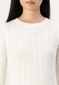 Cream knitted sweater with a ribbed texture, featuring a cable design and a crew neckline. Long sleeves seamlessly integrated into the body.