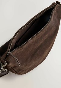 Braune Wildleder-Crossbody-Tasche mit einem Reißverschluss und Innenfach, ausgestattet mit silbernem Zubehör und einer weichen, strukturierten Oberfläche.