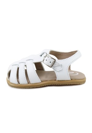 Sandalia para niño pequeño de cuero blanco con punta cerrada, correa ajustable con hebilla, laterales abiertos y suela de goma color tostado.