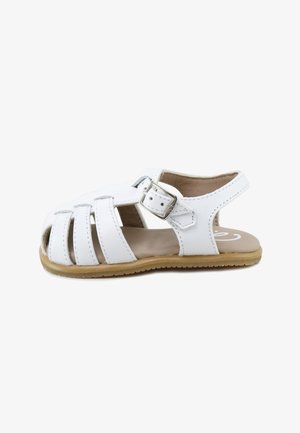 Sandalia para niño pequeño de cuero blanco con punta cerrada, correa ajustable con hebilla, laterales abiertos y suela de goma color tostado.