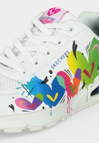 Λευκό αθλητικό παπούτσι Skechers με λευκά κορδόνια, διακοσμημένο με πολύχρωμες καρδιές σε στυλ γκράφιτι και το λογότυπο Skechers στο πλάι και στη γλώσσα.
