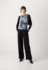 Long-sleeve shirt with a colorful graphic pattern, paired with wide-leg black trousers and pointed black heels. Simple bag accentuates the look.