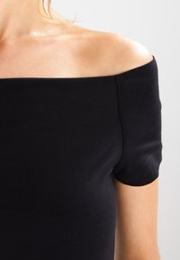 Černý top na jedno rameno s krátkými rukávy, vyrobený z hladké, elastické tkaniny. Jednoduchý design s přiléhavým střihem a švy.