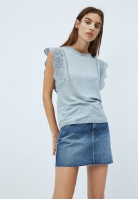 Top gris claro de manga corta con detalles de encaje festoneado en las mangas, combinado con una falda corta de mezclilla azul con bajo deshilachado.