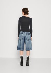 Top negru cu mânecă lungă și textură plisată, asociat cu pantaloni scurți Bermuda din denim de un albastru mediu, cu manșete răsucite și buzunare în partea din spate. Botine negre completează look-ul.