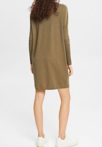 Robe tricotée vert olive à manches longues, coupe ample et encolure ronde, arrivant mi-cuisse, associée à des baskets blanches.