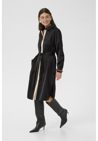 Rochie din satin neagră, cu placket bej la nasturi, talie cu curea, slituri laterale și mâneci lungi. Purtați cu cizme negre până la genunchi.