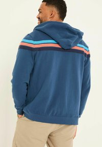 Navy blue hooded sweatshirt featuring horizontal stripes in light blue, coral, and dark blue across the upper back. Soft fabric texture.