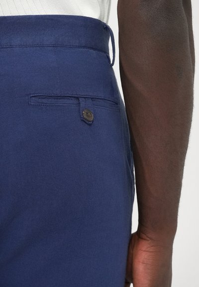 Tengerészkék nadrág texturált anyagból, övhurkokkal, fekete gombos hátsó zsebbel és egyenes szabással.