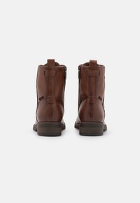 Un par de botines de cuero marrón vistos desde atrás, con cremalleras laterales y lengüetas, descansando sobre un fondo blanco.