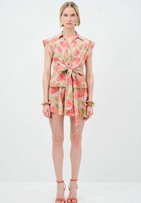 Abito a camicia floreale con maniche corte e fiocco frontale, caratterizzato da fantasie di foglie rosa e verdi. Realizzato in tessuto leggero, abbinato a sandali con cinturino.