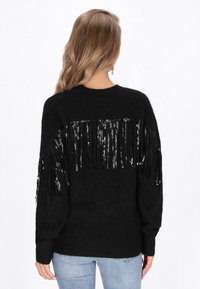 Maglione nero realizzato in materiale morbido, caratterizzato da un design di paillettes frangiate sul retro. Maniche lunghe e scollatura rotonda.
