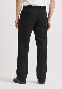 Schwarze Jogginghose aus weichem Stoff, mit einem elastischen Bund und zwei Gesäßtaschen. Die Passform ist locker mit geradem Bein.