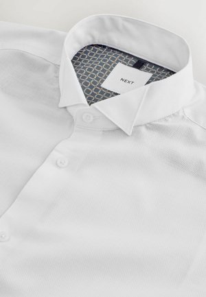 Camicia bianca button-up con tessuto testurizzato, colletto classico e interno a motivo blu e oro nel colletto e nell'etichetta.