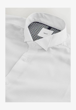 Biała koszula z guzikami, wykonana z teksturowanej tkaniny, z klasycznym kołnierzykiem i wzorzystym niebiesko-złotym wnętrzem kołnierza oraz metki.
