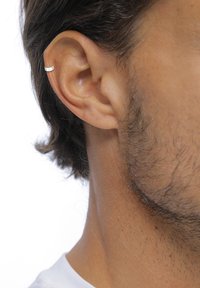Boucle d'oreille en argent visible dans l'oreille, présentant une surface lisse et polie avec un design circulaire. Le teint est clair avec quelques poils au visage.