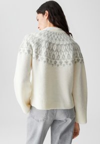 Maglione di lana color crema con un motivo geometrico grigio a trama sulle spalle e polsini a costine. Design accorciato con una vestibilità rilassata.