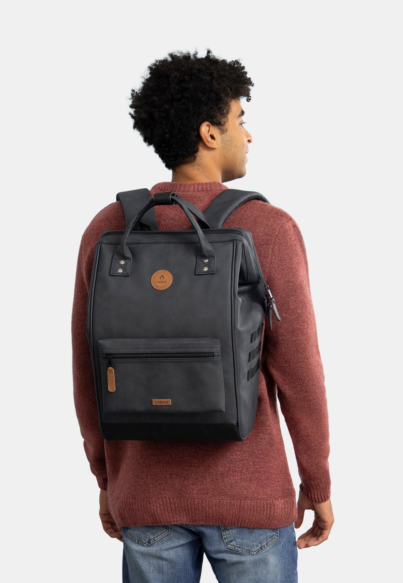 Sac à dos noir au design structuré, en matériau imitation cuir brillant, avec poche avant zippée et détails en marron. Bretelles réglables.