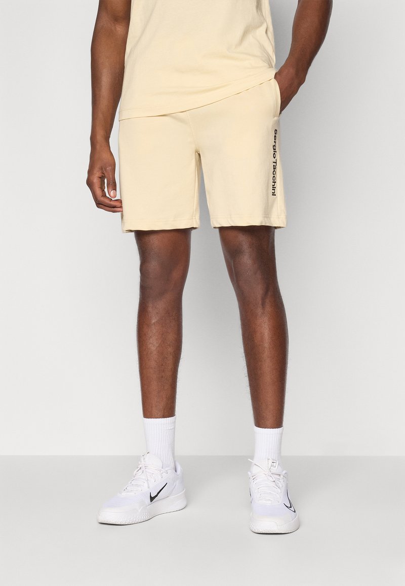 Beiga bomullsbyxor med elastisk midja och sidofickor, med "Sergio Tacchini" tryckt i svart på vänster sida.