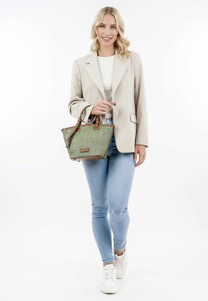 Sac à main tissé vert avec des accents en cuir marron, des poignées supérieures et un design structuré. Le modèle porte un jean clair et un blazer beige.