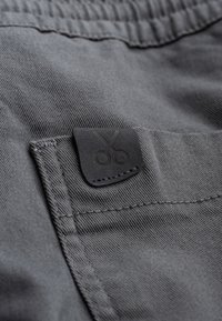 Grijze stof met een gladde textuur heeft een zwart leren patches met een schaarontwerp. Stiksel is zichtbaar langs de randen.