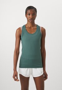 Green athletic tank top with a scoop neck, featuring light pink straps. The fabric is smooth with a fitted design, paired with white shorts.