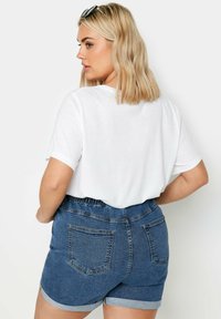 Camiseta corta blanca combinada con pantalones cortos de denim azul, con cintura elástica y dobladillos enrollados. Tejido suave con bolsillos traseros.