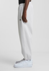 Lys grå sweatpants med elastisk talje og manchetter. Har et lille sort logo på siden. Parret med hvide sneakers.