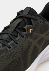 Chaussure de sport noire avec un dessus texturé, accents orange contrastants et semelle blanche. Les languettes s'intègrent à des superpositions en tissu à motifs.