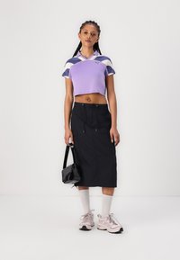 Camisola polo roxa corta com detalhes em azul-marinho e branco, combinada com uma saia midi preta, meias brancas e ténis rosa claro. Inclui uma bolsa preta.