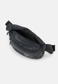 Musta nylonselkäpussi, jossa on vetoketjukiinnitys. Varustettu tekstuuripinnalla ja säädettävällä hihnalla. Sisäpuoli on sileä ja tilava lokero.