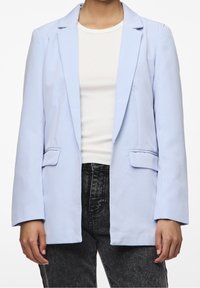 Světle modrý blazer z hladkého materiálu, s dlouhými rukávy, dvěma předními kapsami a volným střihem. Nositý přes bílý top.