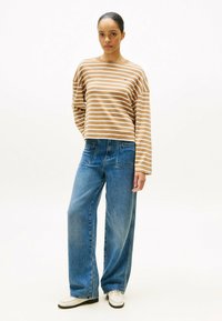 Stripet beige og hvid langærmet skjorte parret med løse blå jeans. Bemærkelsesværdige detaljer inkluderer en frontlomme og syede sømme.
