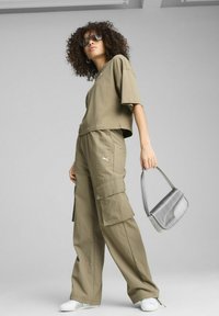 Khaki oversized majica s kratkimi rokavi in cargo hlačami, ki imajo več žepov. Drži srebrno torbico z teksturo. Bele teniske.