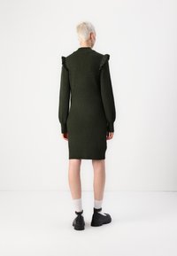 Robe en tricot vert foncé, avec des manches longues agrémentées de volants. La coupe est ajustée, s'étendant jusqu'à mi-cuisse. Texture lisse.