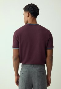 Bordo trumpomis rankovėmis polo marškinėliai su faktūruota medžiaga, turintys mėlynos ir baltos spalvų dryžuotą apykaklę. Dėvimi su pilkais faktūruotais kelnėmis.