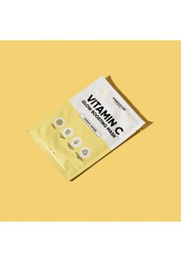 Un emballage jaune pour un masque boosteur d'éclat à la vitamine C présente une étiquette blanche avec du texte noir et des icônes, indiquant les ingrédients et les bienfaits.