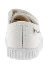 Scarpa slip-on bianca in tela con suola in gomma texturizzata, caratterizzata da dettagli cuciti e una piccola etichetta "victoria" multicolore sul tallone.