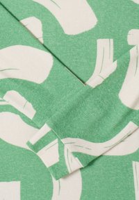 Tissu en coton vert présentant un motif blanc audacieux et abstrait avec des formes courbes. Texture douce avec des détails de couture visibles.