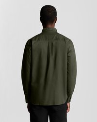 Camisa de botonadura en verde oliva oscuro con cuello, detalles de pliegue en la parte posterior y mangas largas. Presenta una textura suave y puños con botón.