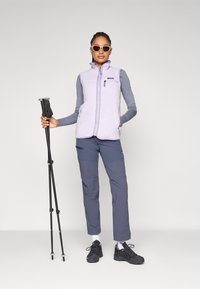 Gaiši purpura vilnas veste ar rāvējslēdzēju, apvienota ar pelēku garām piedurknēm topu un tumši pelēkiem trekinga biksēm. Melni pārgājienu apavi un trekinga nūja iekļauti.