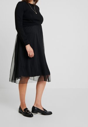 Sort, langærmet top kombineret med et midt-langt, flydende sort tylskørt. Bruges med sorte loafers med en cirkulær detalje.