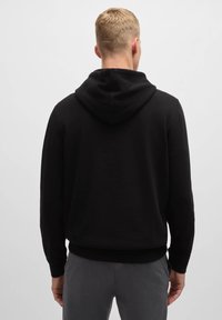 Svart hoodie gjord av mjukt, texturerat material, med en dragsko i huvan, ribbade ärmslut och nederkant, samt en avslappnad passform.