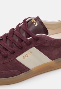 Burgundy suede sneaker with a smooth beige panel, gold lettering, and matching laces. Features a clear rubber sole with a textured pattern.