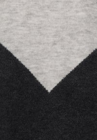 Szara i czarna dzianina z wzorem w kształcie litery V. Górna szara część jest miękka, podczas gdy czarna dolna część ma lekko teksturowane wykończenie.